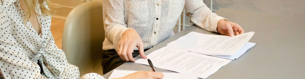 woman signing on white printer paper beside woman about to touch the documents